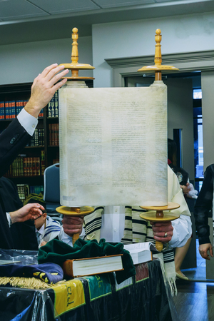 A Jewish man lifts a Torah scroll as he takes part in a Shacharit prayer a group of Orthodox Jews...