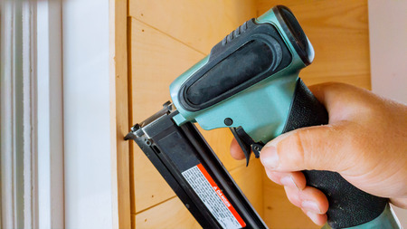Carpenter brad using nail gun to moldings on windows, framing trim, with the warning label that all power toolsの写真素材