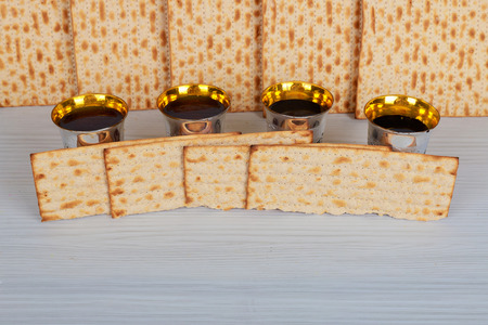 Pack of matzah or matza, Passover Haggadah and Kosher red wine on four cups a vintage wood background. Jewish Passover holiday composition with copy space.の写真素材
