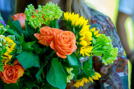 Young woman holding modern asymmetrical bouquet of flowers on the a sunflower in front of the fieldの写真素材