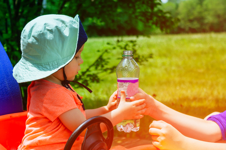 Mother gives to baby girl to drink water from a bottle in a park. child drinks and looking at the a bottle outdoor.の写真素材