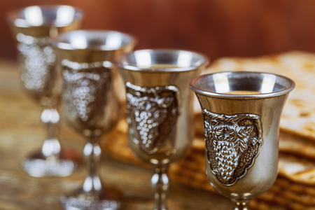 Symbols of Passover background four glasses wine and matzoh jewish holiday bread over wooden board.の写真素材