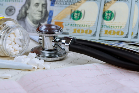 Medical stethoscope on cardiogram with pills and dollars healthy life conceptの写真素材