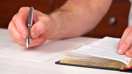 Man is holding a pen in his hand with an open book lying in fornt of him Sunday readings, Bibleの写真素材
