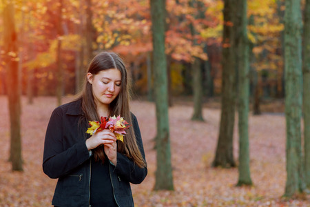 Young girl smiling holding orange leaves in hands in autumn park in the forest