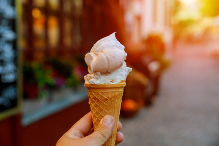 Person walking along the road with an ice cream in his hands, shallow depth of field.