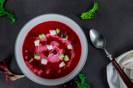 Bowl of cream soup of red beets with a fresh beet root and leaves on rustic tableの写真素材