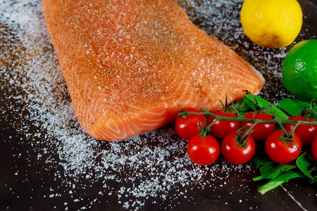 Raw salmon steaks on dark board marinated with herbs and spices