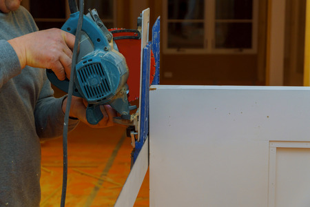Worker is holding in hands electric circular saw cutting door profile close up industry production.の写真素材