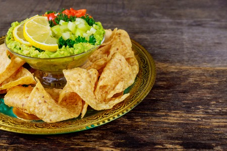 Guacamole with tortilla chips in fresh ingredients over vintage rusty a bowl on a dark wood...