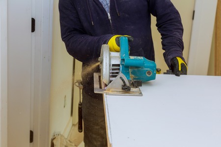 Man's hands holding circular saw and preparing to make a cut in doorの写真素材