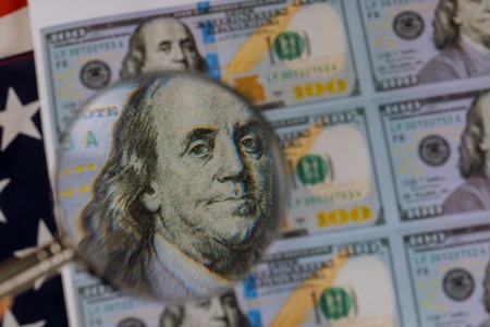 US dollars and magnifying glass on a print counterfeiting fake money currencyの写真素材
