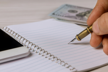 Male hand writes a pen in notepad the dollars, smartphone business conceptの写真素材