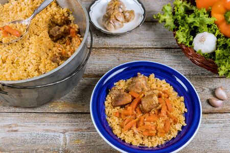 Traditional uzbek meal pilaf rice with meat, carrot and onion in plate on vintage wooden backgroundの写真素材