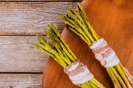 Green fresh asparagus wrapped with bacon on wooden plate.の写真素材