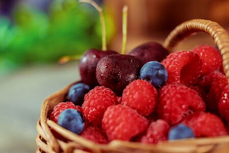 Raspberries and blueberries in a basket and couple cherriesの写真素材