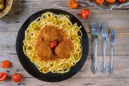 Spaghetti and meatballs with tomato sauce in black dish on wooden background with red pepperの写真素材