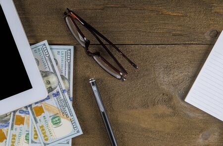 Eyeglasses on tablet pc with money dollar bills and pen on wooden table at close upの写真素材