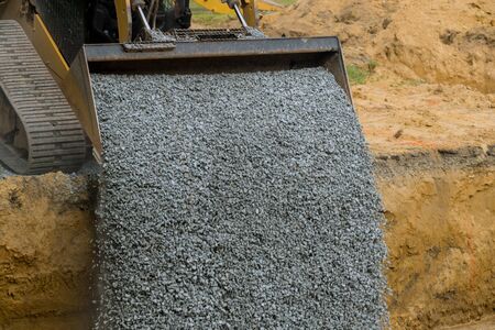 Excavator bucket backfilling trench for stone backfill of foundation excavator bucket working