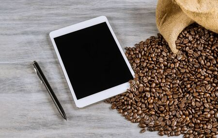The tablethone and pen lies next to coffee beans on table.の写真素材