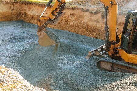 A yellow excavator moving gravel in the foundation in the house poles on gravel