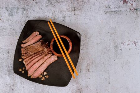 Asian grilled steak with soy sauce and chopstick in black plate.