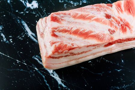 Pork pieces fat layers with meat of raw belly on a black stone backgroundの写真素材