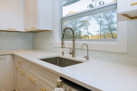 Stainless steel kitchen sink and window centered in a modern kitchen faucetの写真素材