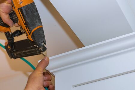 Air nailer tool close up of carpenter using nail gun to crown moldings on kitchen cabinets with white cabinetsの写真素材