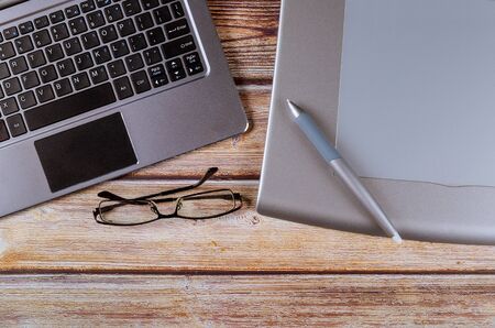 Graphic designer workspace with a pen tablet, a computer laptop and glasses