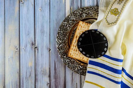 Matzoh jewish passover bread in the traditional seder plate with kipah and tallit over wooden table