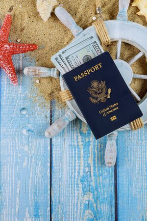 Sailor's captain's wheel summer time to travel concept sea shells in the beach sand over hundred dollar bills American Passportの写真素材
