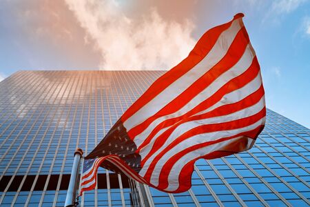 American flag on flagpole waving in the wind against clouds
