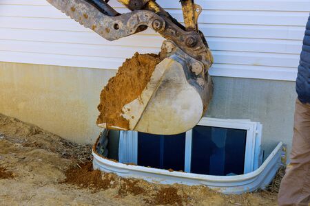 Excavator moving earthmover in the new house under construction window well craft basement...