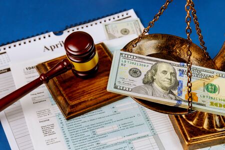 Hundred US dollar bills on a table scales of justice, gavel IRS form. 1040 U.S tax forms calendar while pages April of the deadline time tax seasonの写真素材