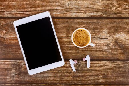 Workplace modern gadgets white digital tablet coffee cup of espresso on wireless headphones with wooden tableの写真素材