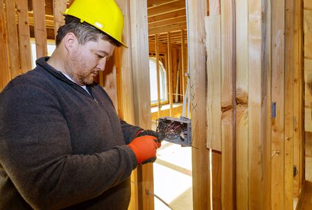Electrician routing wires in electric plug connector, electric sockets on the wall inside a wooden beams frame houseの写真素材