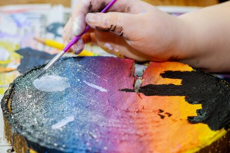 Girl draws uses colored paints brushes a picture in woodenの写真素材