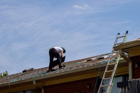 Roof repair, worker with replacing gray tiles shingles on house being applied