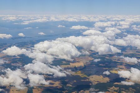 Airplane flying above clouds over beautiful green grass fields land above is the blue sky