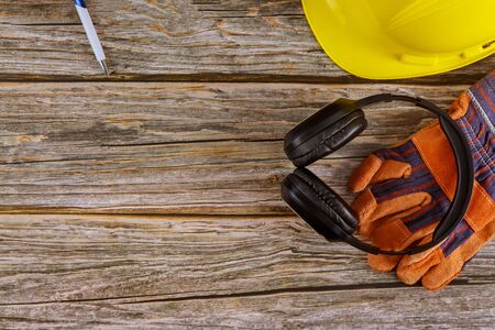 Standard construction safety equipment earmuffs leather safety helmet protective gloves on wooden...