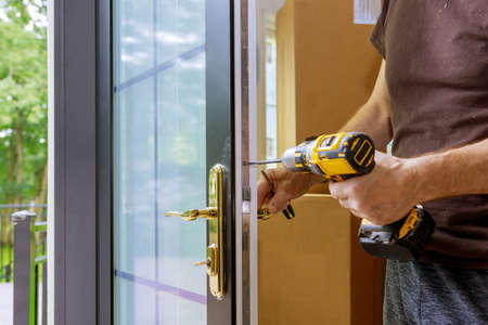 Install the door handle with a lock, Carpenter tighten the screw, using an electric drill screwdriver, close-up.の写真素材