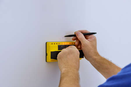 Man hand is scanning wall by uses Multi-Sense Technology to find studs more accurately through...