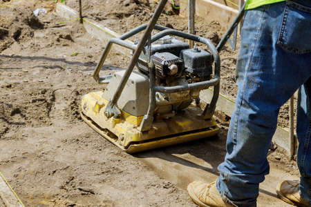 Worker use vibratory plate compactor under construction at soil on new pavement