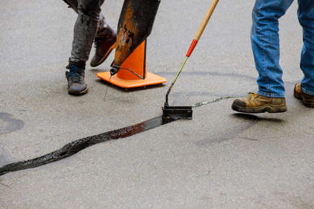 Road surface restoration work in the worker performs on road patcher work on the repair of cracks by filling and sealing with coated by bitumen emulsion asphalt surface.の写真素材
