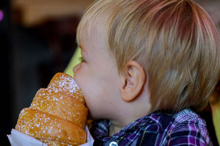 Close up hand little boy having breakfast in cafe in beautiful kid eating croissant bun chocolate the table in restaurant eco paper bag.の写真素材