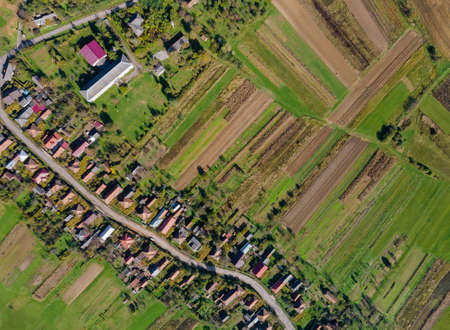 Aerial view from the height of the beautiful of rural village with houses and streets on plowed fields, meadowsの写真素材
