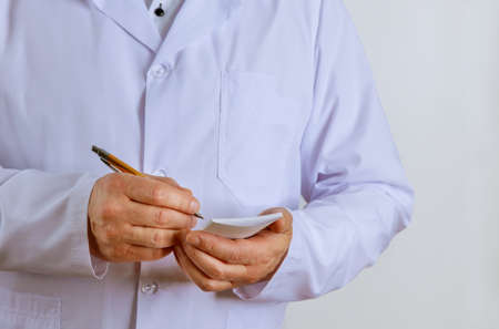Male doctor in white medical uniform make notes prescription in write patient medical at...
