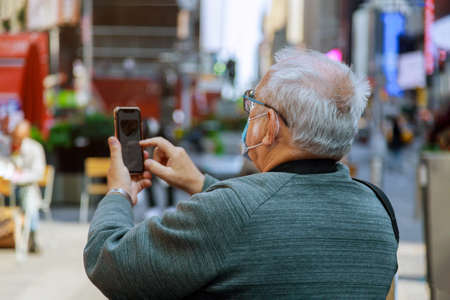 Man traveling looking at in smartphone of Times Square, Manhattan, New York City on wearing a face...