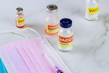 Vaccine bottle CoronaVirus SARS-CoV-2 and syringe, on a protective surgical mask, medical syringe